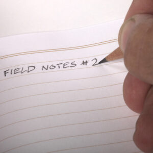 Hand schreibt mit Bleistift ins Notizheft